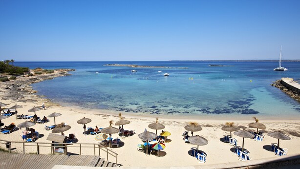 A beach with clear blue water, umbrellas, and lounge chairs. - Universal Hotel Marqués (Ses Salines)