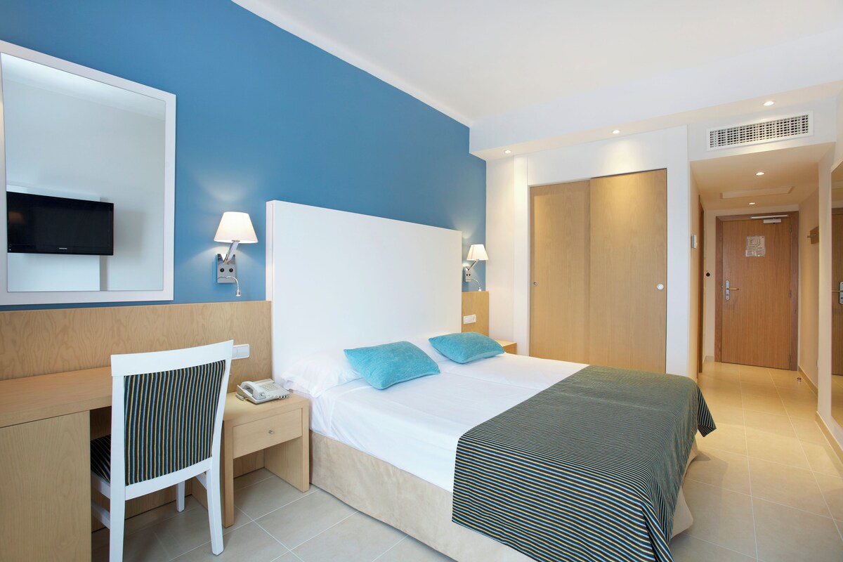 A hotel room with a bed, a desk, a chair, a TV, and a wardrobe.