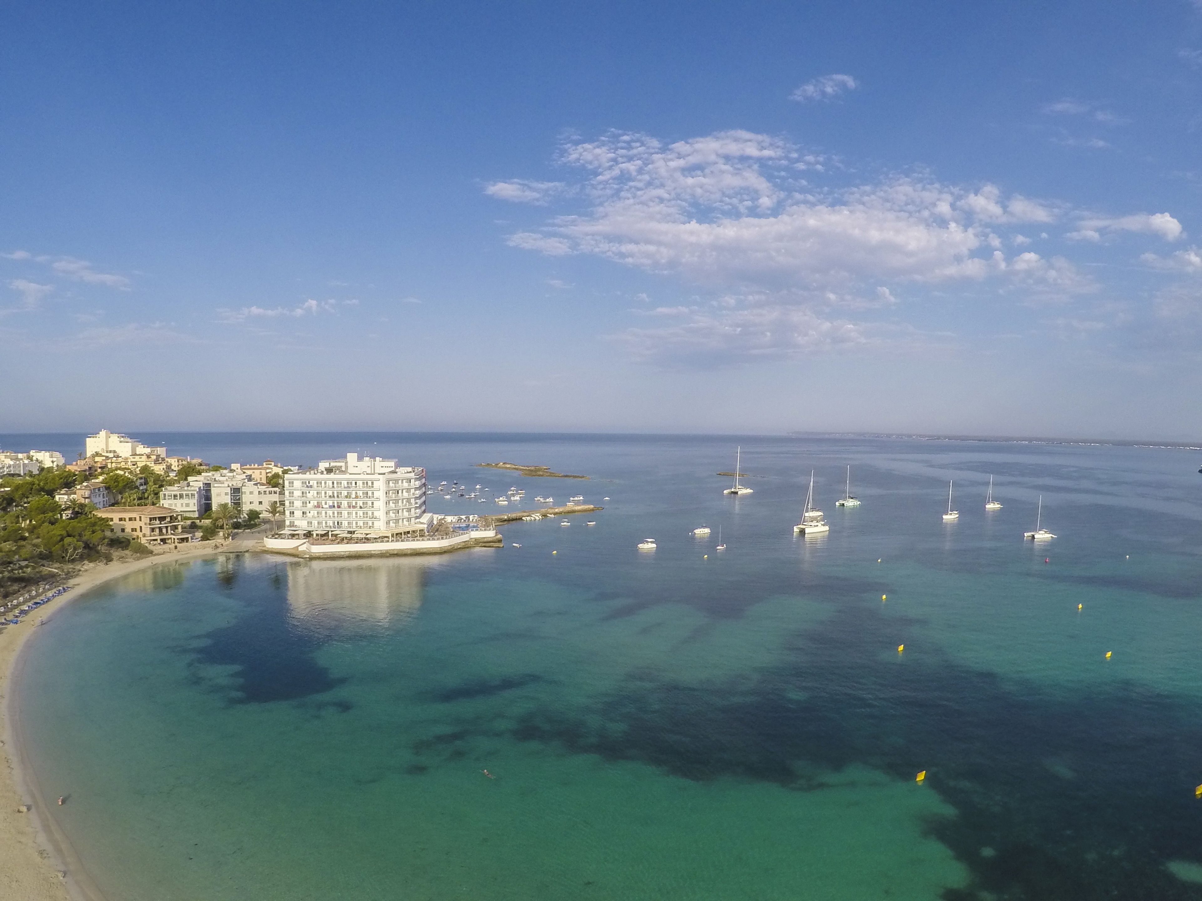 Una zona costera con un puerto deportivo, aguas turquesas cristalinas y edificios a lo largo de la orilla.