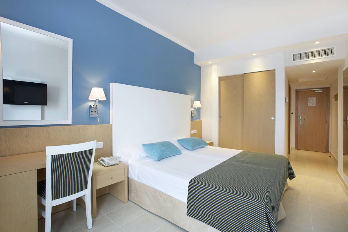 A hotel room with a bed, a desk, a chair, and a TV mounted on the wall.