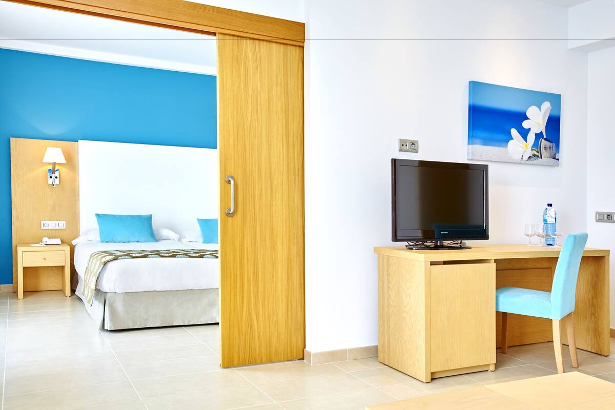 A hotel room with a bed, a desk with a chair, a television, and a painting on the wall.