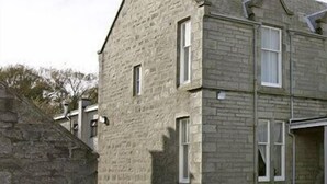 Un bâtiment en pierre doté de nombreuses fenêtres et d’une extension moderne avec de grandes portes vitrées.