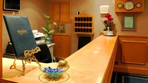 Un comptoir d’accueil avec une chaise bleue, un bol en verre contenant des objets bleus, une horloge et un certificat encadré accroché au mur.