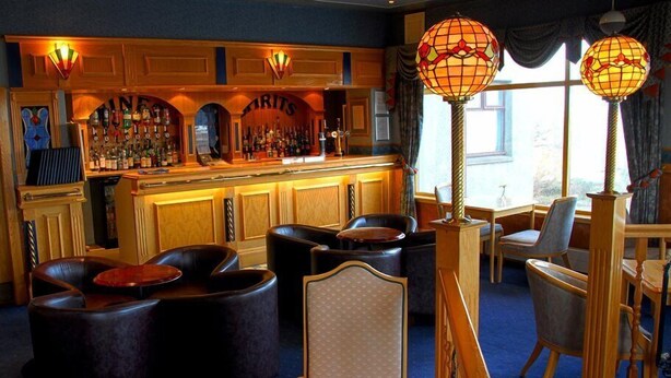 Un espace bar doté d’un comptoir en bois, de sièges en cuir et de lampes décoratives.