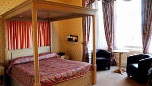 Un lit à baldaquin avec une couvre-lit à motifs, une table de chevet, une chaise et une petite table ronde.
