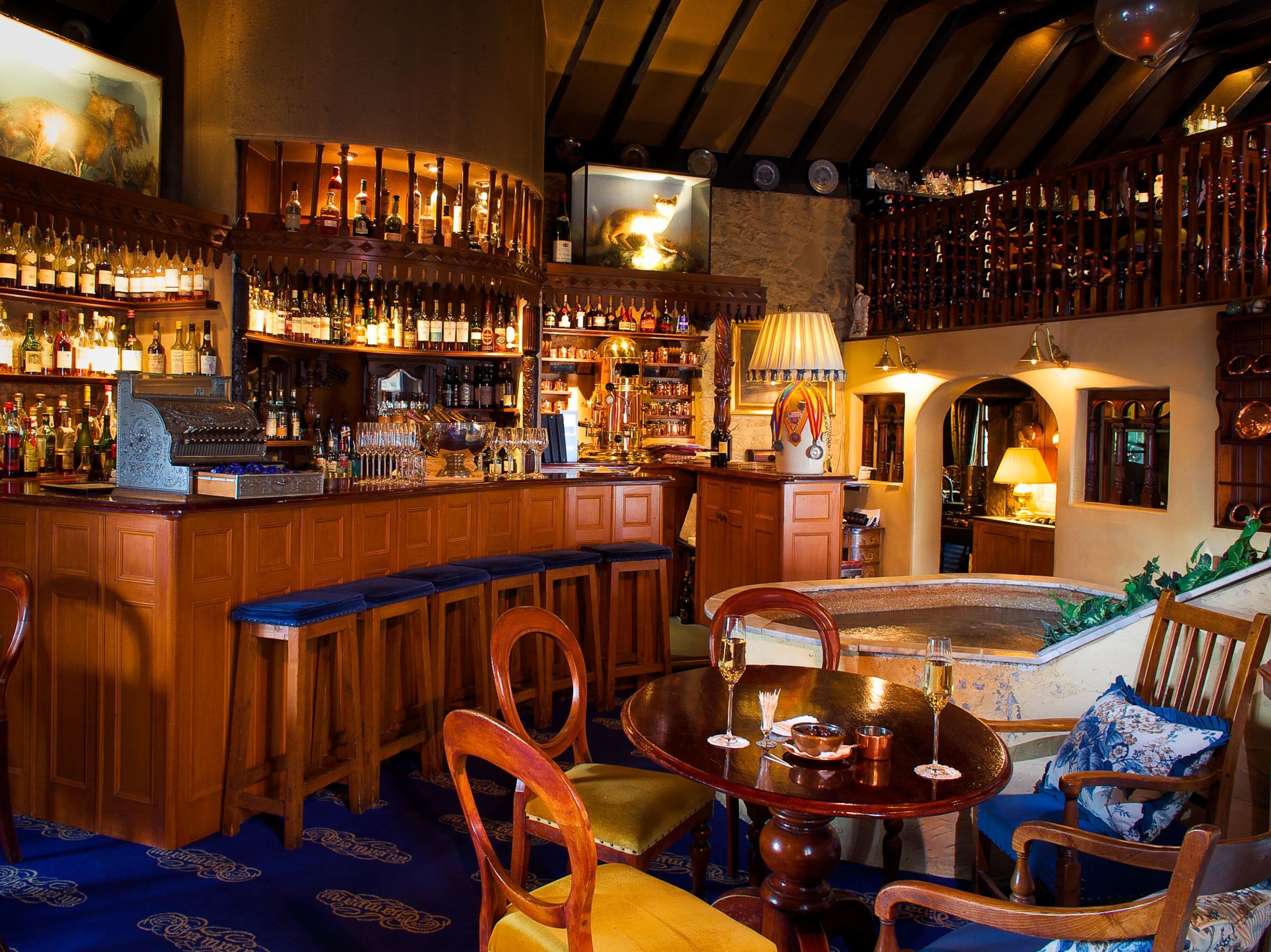 Zona bar con arredi in legno, bancone bar e una selezione di bottiglie e bicchieri.