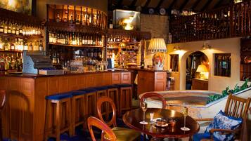 Zona bar con arredi in legno, bancone bar e una selezione di bottiglie e bicchieri.