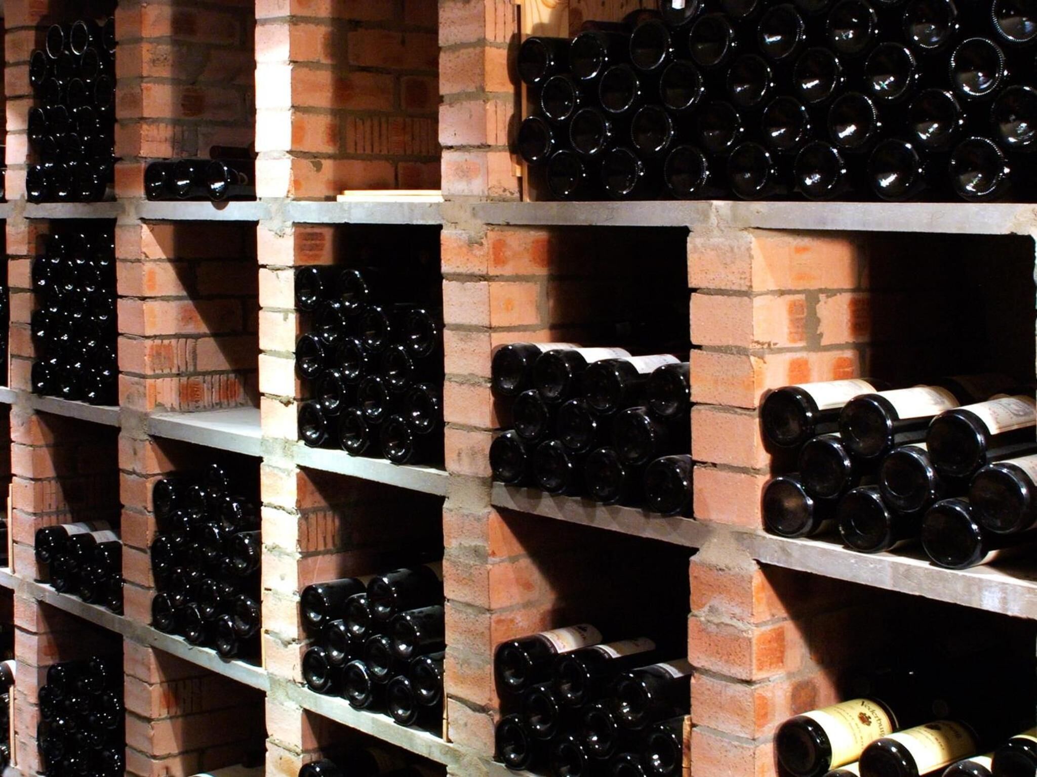 Una bodega con hileras de botellas de vino en estantes frente a una pared de ladrillo.