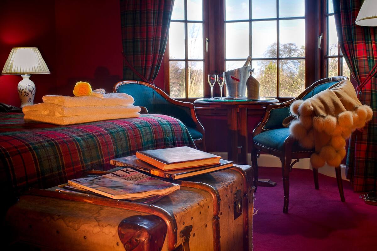 A room with a bed, a table with a bucket, a chair, a suitcase, and a teddy bear.