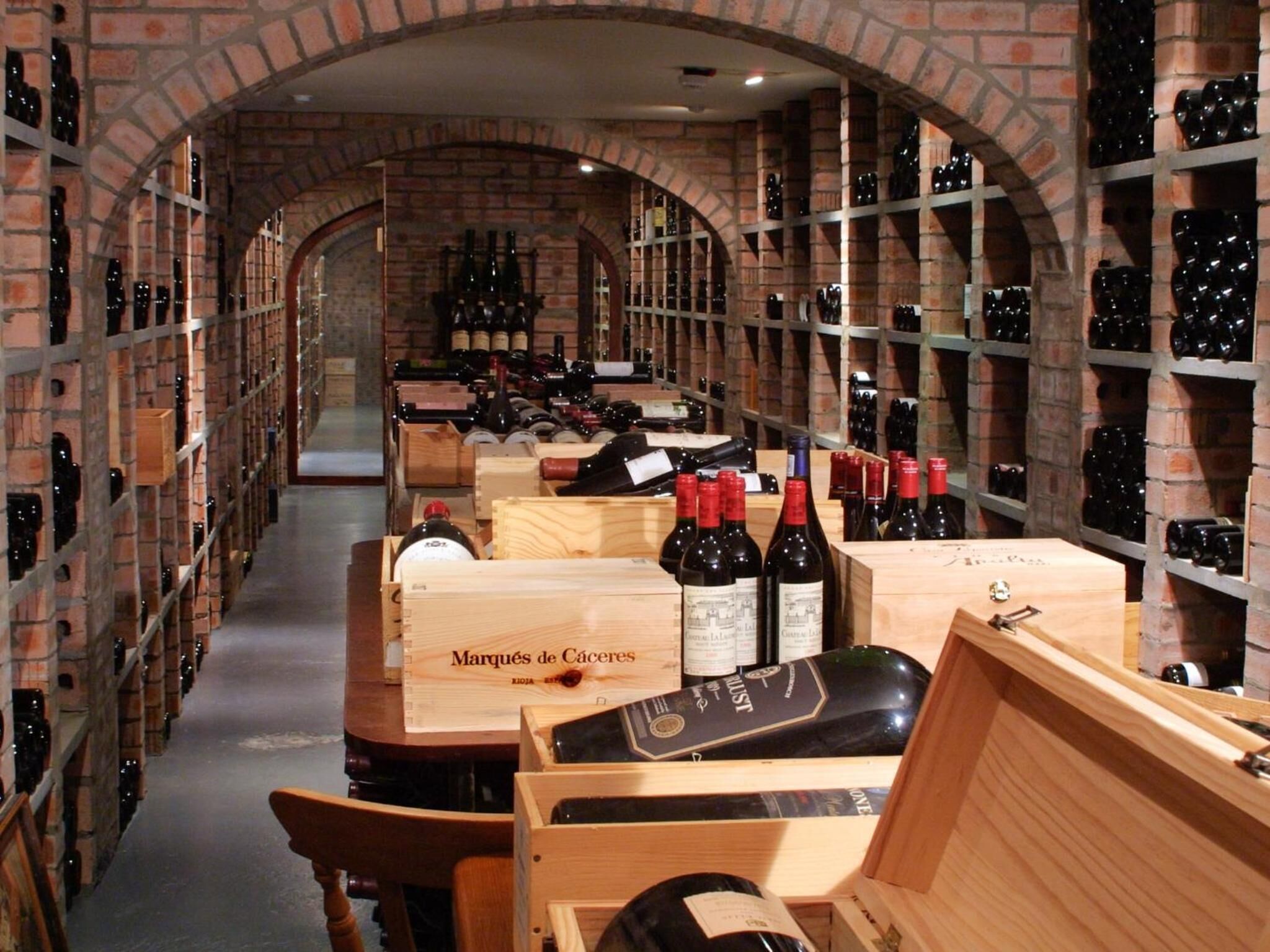 A wine cellar with wooden crates and bottles, brick walls, and arched ceilings.