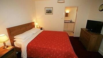 Une chambre à coucher comprenant un lit, une table de chevet, une commode, un téléviseur et une porte donnant sur une salle de bain.