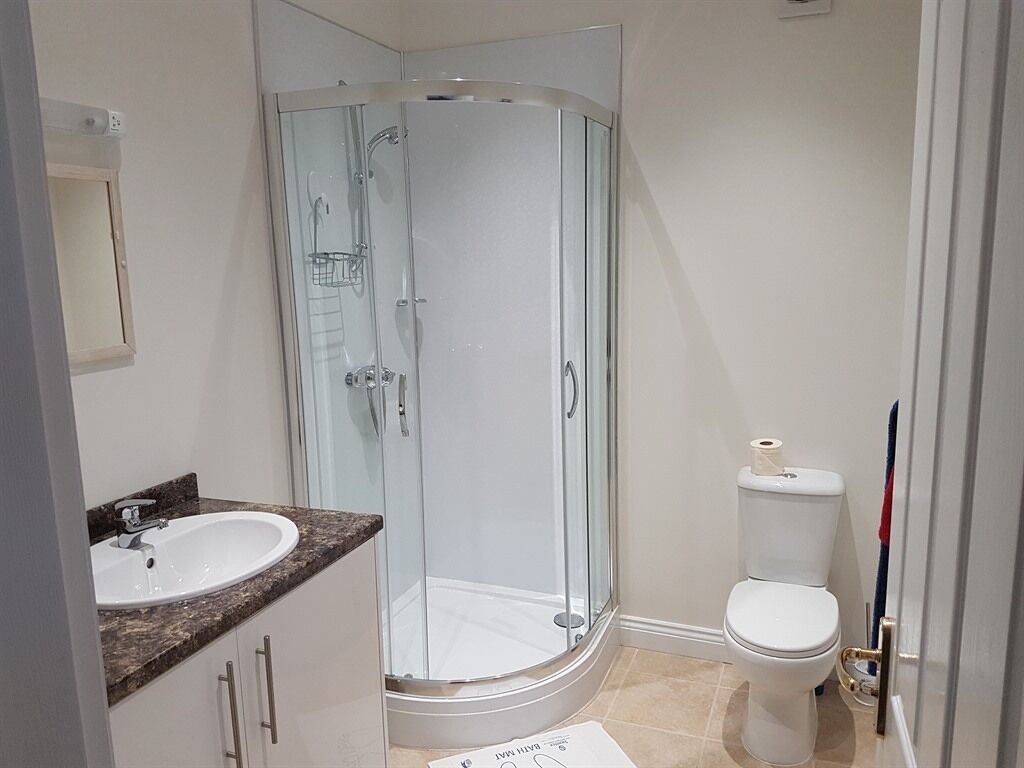 Un baño con cabina de ducha de vidrio, inodoro blanco y lavamanos con encimera de mármol.