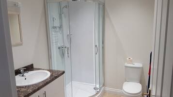 Un baño con cabina de ducha de vidrio, inodoro blanco y lavamanos con encimera de mármol.