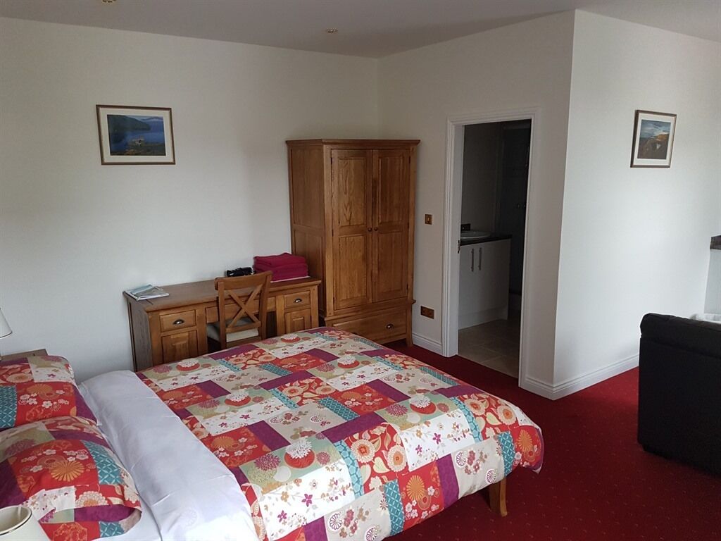 A bedroom with a bed, a desk, a wardrobe, and a door leading to a bathroom.
