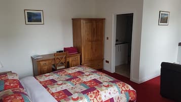 A bedroom with a bed, a desk, a wardrobe, and a door leading to a bathroom.
