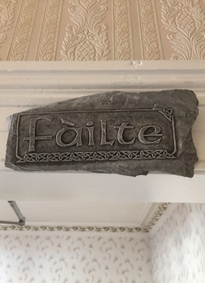A stone plaque with the word "Failte" engraved on it, set against a patterned wallpaper background. - Cameron House Hotel (Oban)