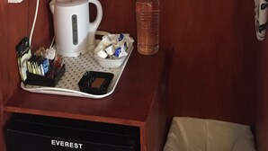 Una kitchenette compacta con cafetera, hervidor y tetera sobre una bandeja, una botella de agua y un basurero con la etiqueta "EVEREST".