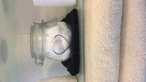 Un frasco de vidrio con cierre metálico en un estante, junto a una toalla blanca y un paño negro.