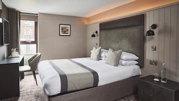 A hotel room with a bed, bedside table, desk, chair, and a window with curtains.