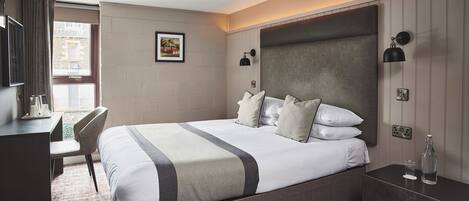 A hotel room with a bed, bedside table, desk, chair, and a window with curtains.