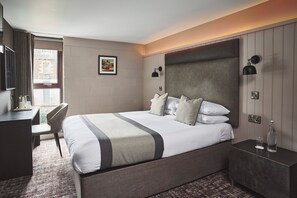 A hotel room with a bed, bedside table, desk, chair, and a window with curtains.