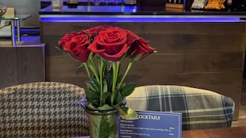 A bar area with a variety of liquor bottles, a menu board, and a vase with red roses on a table.