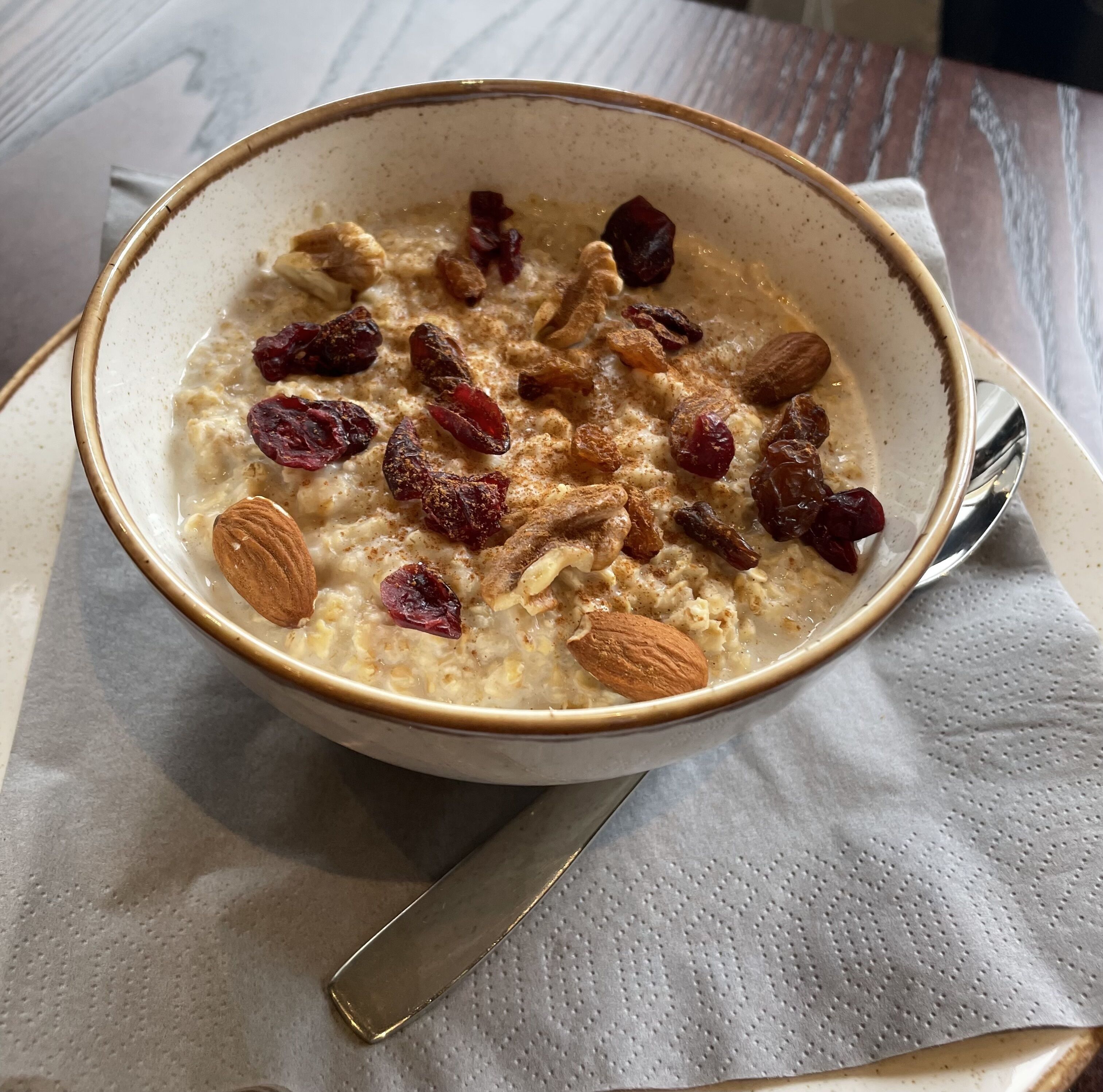 A bowl of oatmeal with almonds and raisins on a napkin.