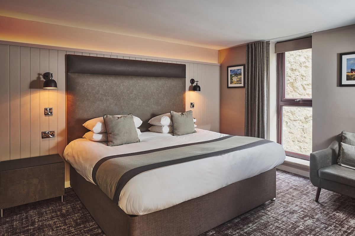 A hotel room with a large bed, bedside lamps, a window with curtains, a chair, and a view of the outside.