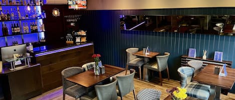 A restaurant with a bar area, wooden tables, and chairs.