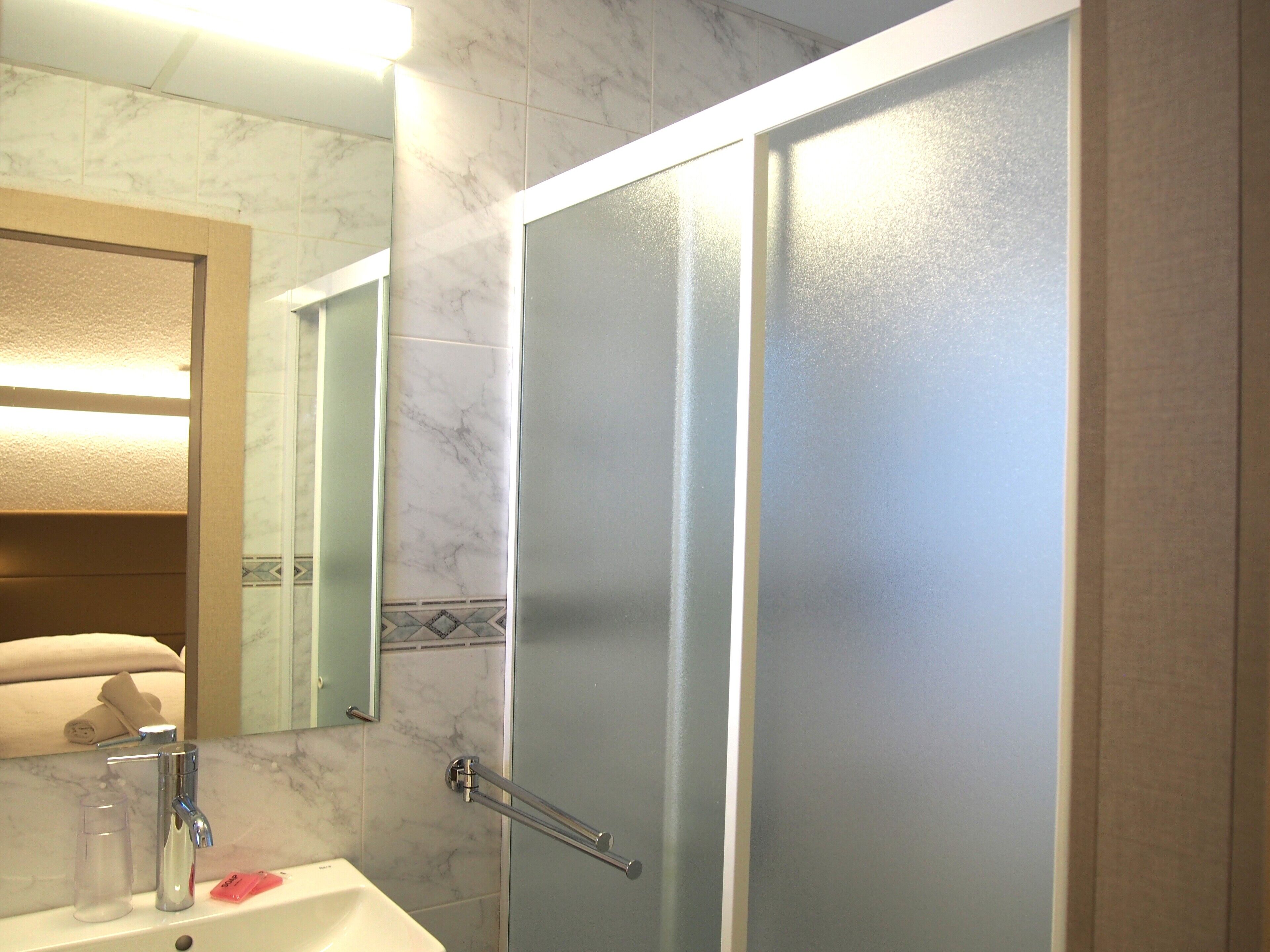 A bathroom with a marble-tiled wall, a sink with a mirror, and a shower with frosted glass doors.