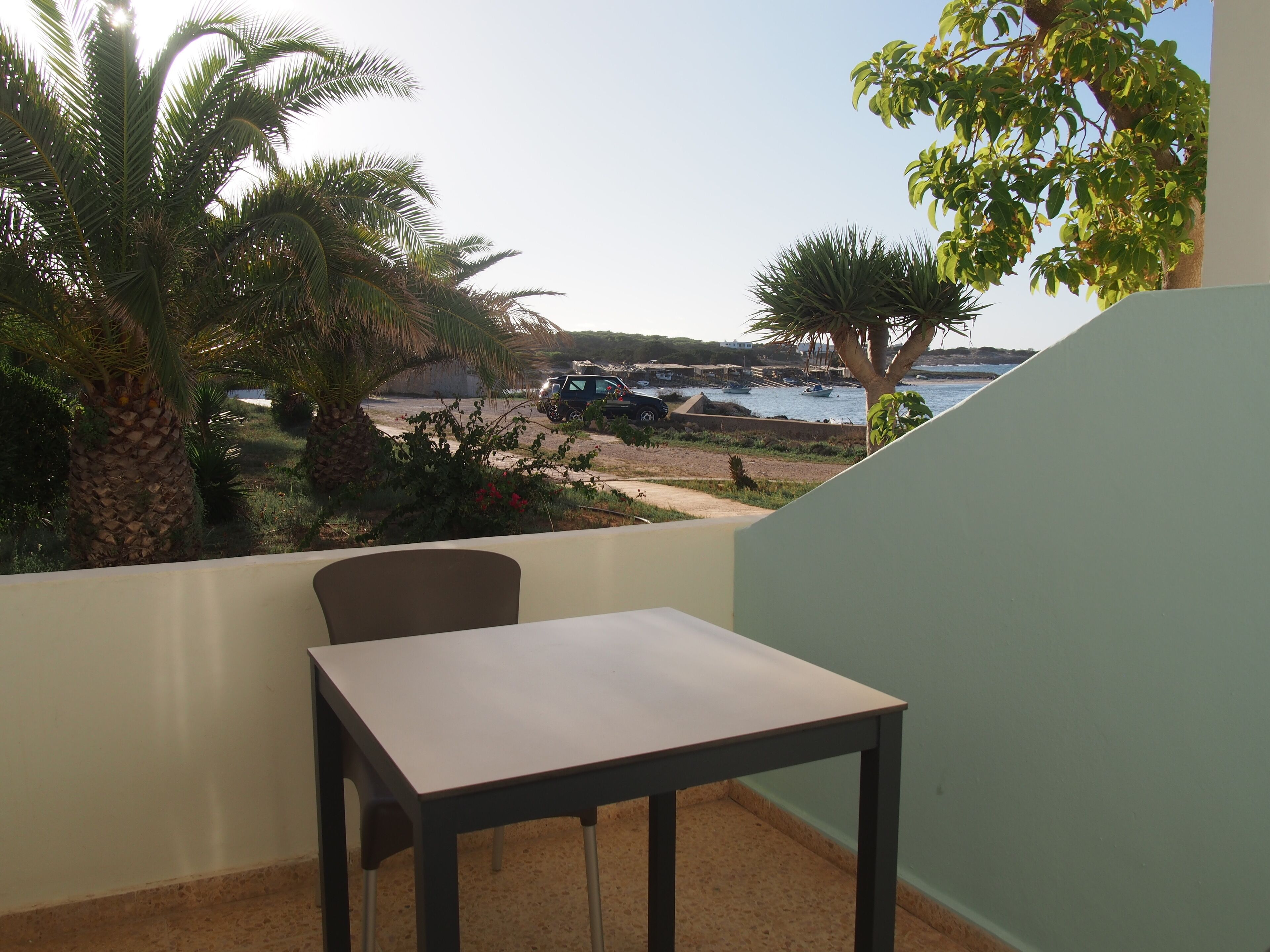 A balcony with a table and chairs, overlooking a marina with boats and a beach.