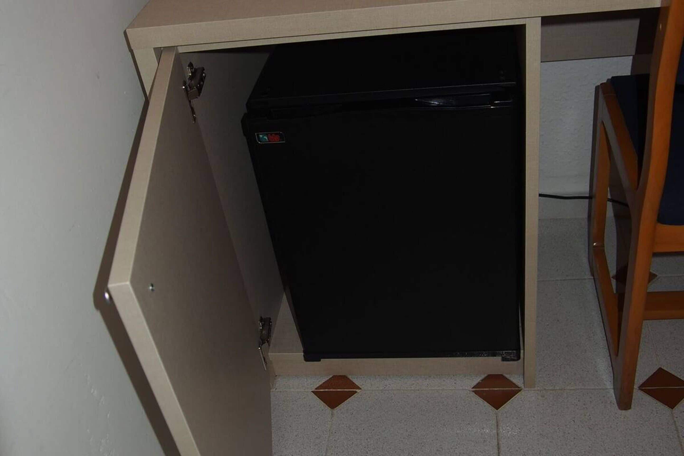 Une cuisine avec un réfrigérateur noir, une chaise en bois et un sol carrelé.