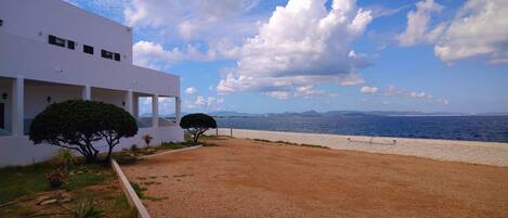 Un edificio moderno con un patio de grava, una valla blanca y vista al mar.