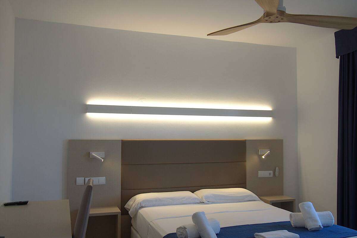Ein Hotelzimmer mit Bett, Nachttischen, Deckenventilator und einer Wandleuchte.