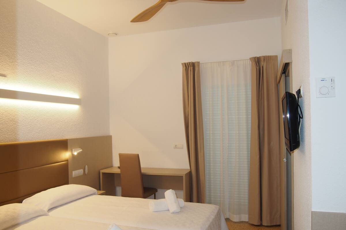 Ein Hotelzimmer mit Bett, Schreibtisch, Stuhl, Fernseher und Vorhängen.
