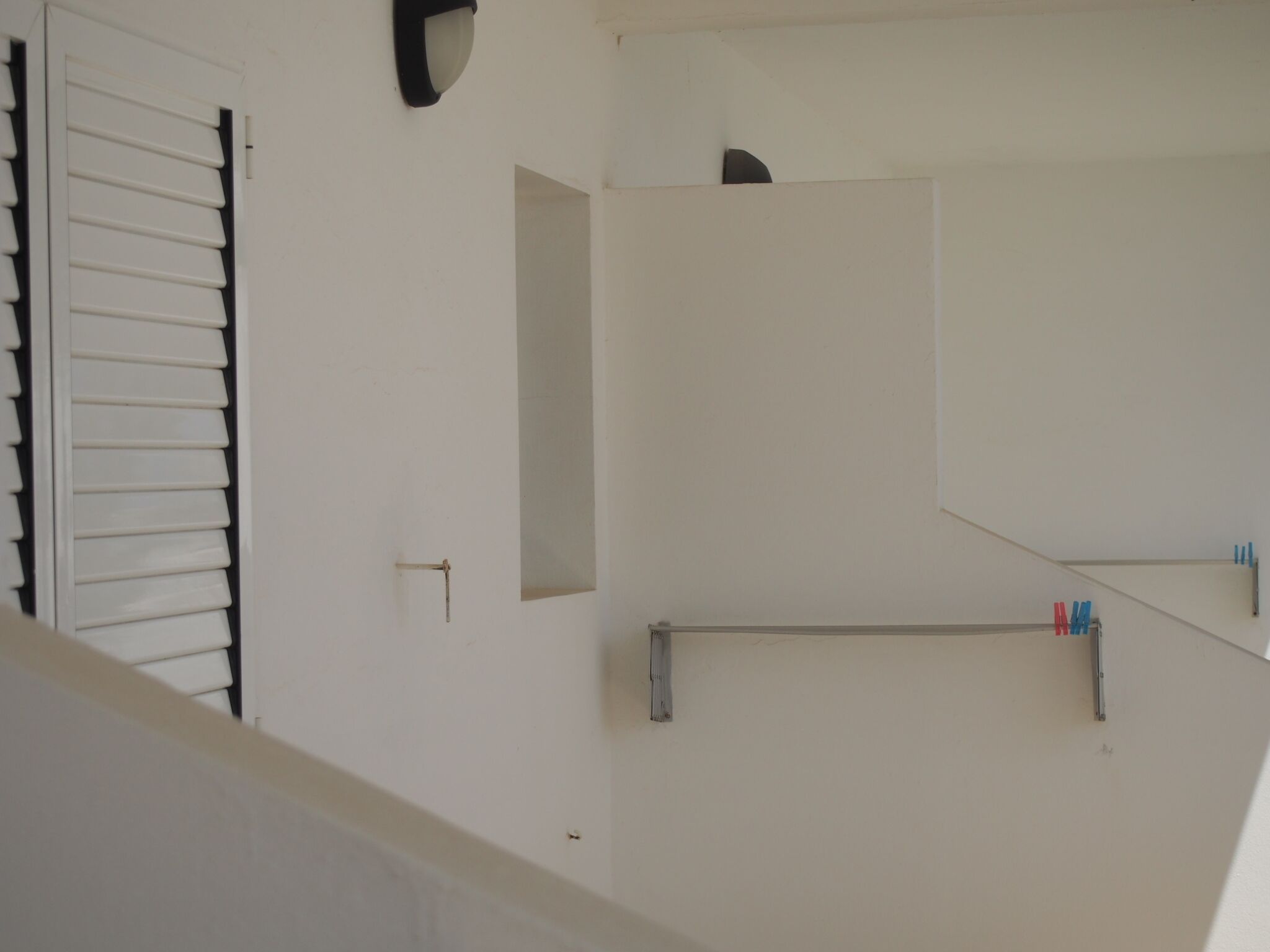 A staircase with a white wall, a door with horizontal blinds, and a small shelf with bottles.