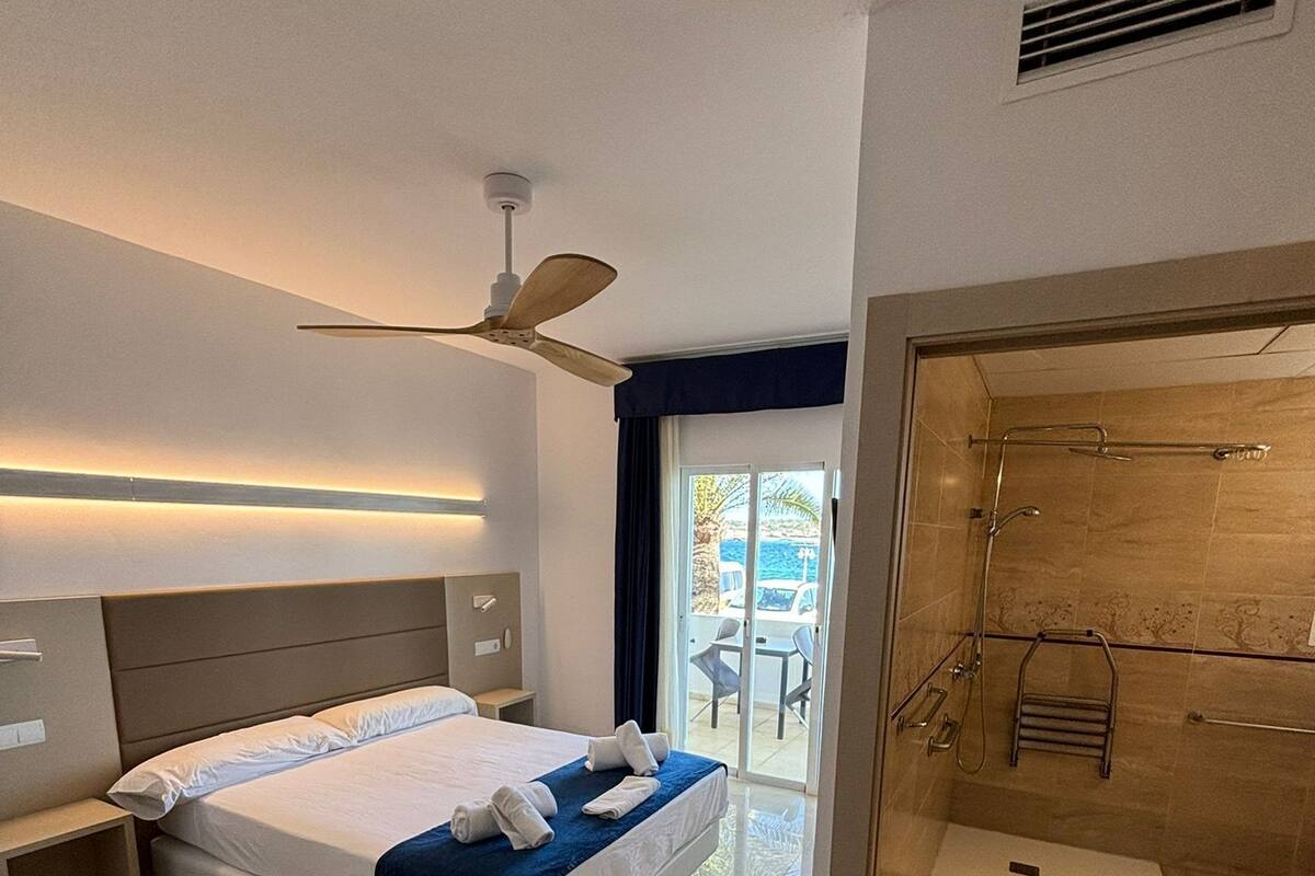 Ein modernes Hotelzimmer mit einem großen Bett, einem Deckenventilator, einem Badezimmer mit Duschkabine und Blick nach außen.