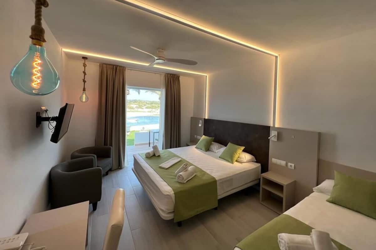Ein Hotelzimmer mit Bett, Schreibtisch, Stuhl, Deckenventilator und Blick ins Freie.