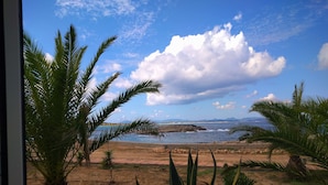 A view from a window overlooking a beach with palm trees and a rocky shoreline.