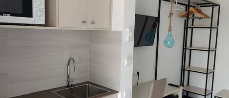 Una cocina compacta con microondas, un lavamanos y una pequeña zona de comedor.
