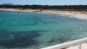 A coastal beach scene with clear turquoise waters, a sandy shore, and a distant building.