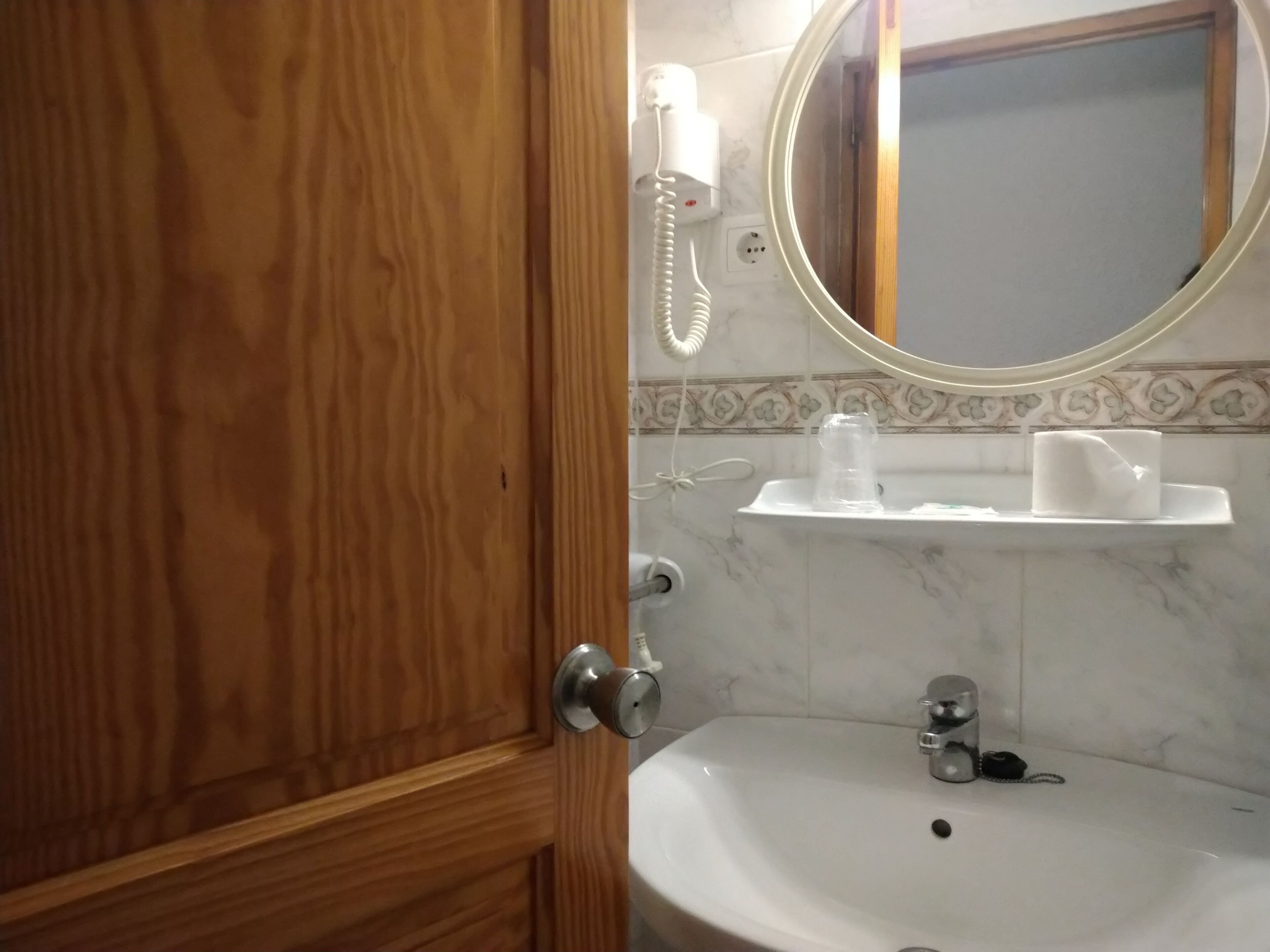 A bathroom with a wooden door, a white sink, a mirror, and a telephone.