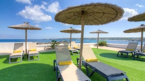 A poolside area with lounge chairs and thatched umbrellas, overlooking a body of water.