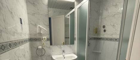 A bathroom with a marble floor, a pedestal sink, a bidet, a handheld showerhead, and a glass-enclosed shower.