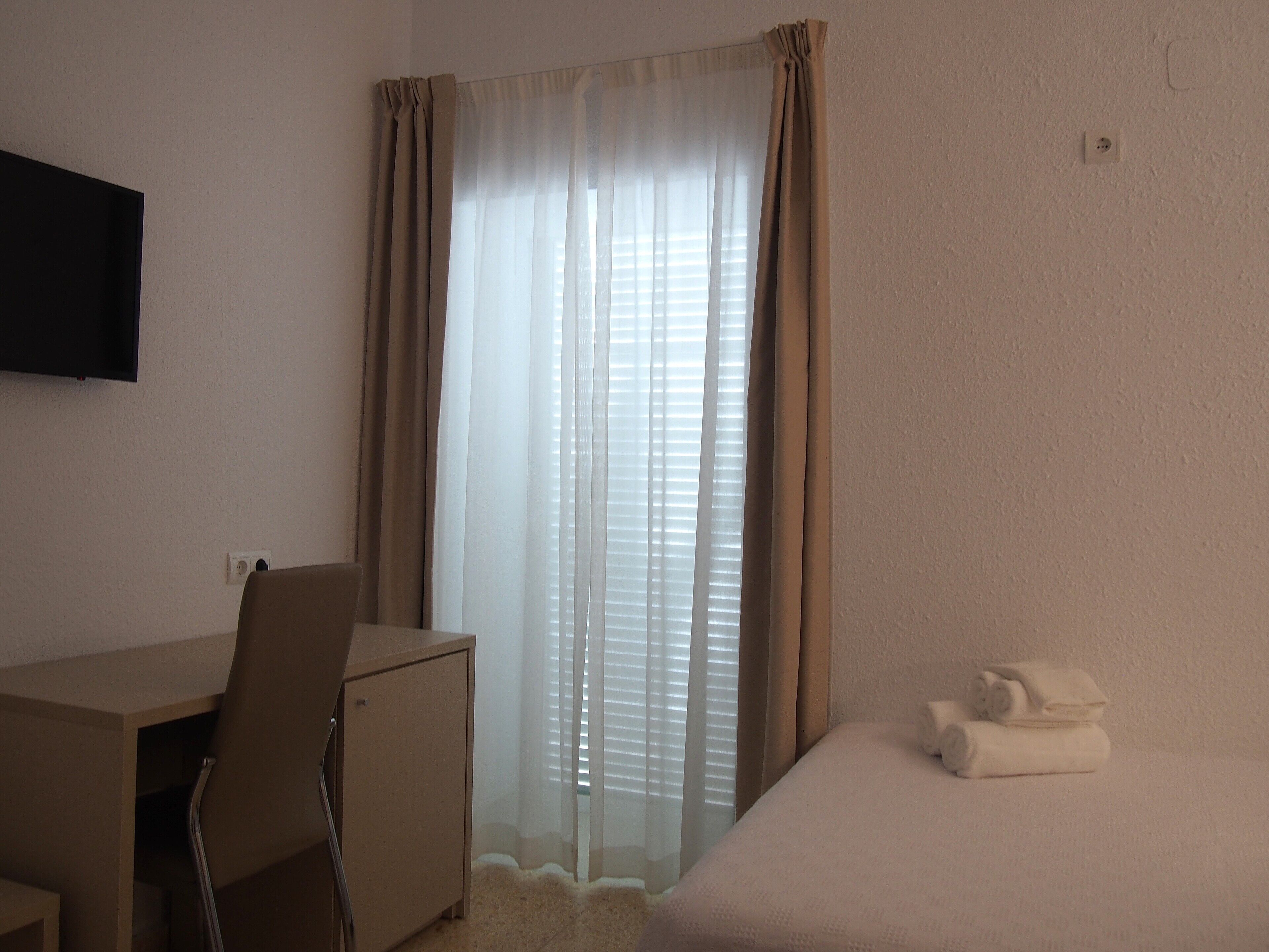 A hotel room with a desk, chair, and a bed with a rolled-up towel.
