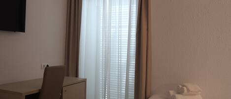 A hotel room with a desk, chair, and a bed with a rolled-up towel.