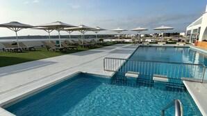 A swimming pool with clear blue water, surrounded by lounge chairs and umbrellas.