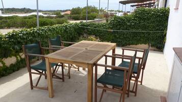 Un patio al aire libre con una mesa y sillas de madera, rodeado de follaje y vistas a edificios en la distancia.