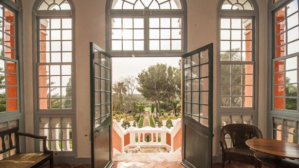 Un vano abierto que da a un jardín con una fuente, rodeado de amplias ventanas y un banco.