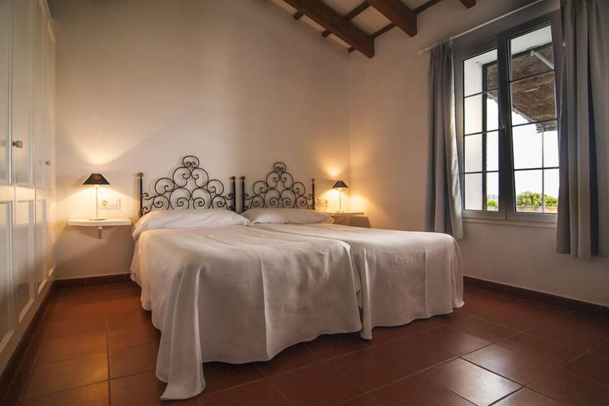 A bedroom with two beds, a decorative headboard, bedside lamps, and a window with curtains.